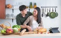 Young Asian sweet couple cooking together in home kitchen. Handsome man helping holding beautiful woman hand slicing bread for Royalty Free Stock Photo