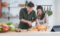 Young Asian sweet couple cooking together in home kitchen. Handsome man helping holding beautiful woman hand slicing bread for Royalty Free Stock Photo