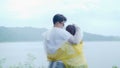 Young Asian sweet couple feeling happy using romantic time playing rain while wearing raincoat standing near lake. Lifestyle