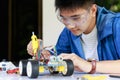 Young asian teen plugging electric wire and signal cable to sensor chip of toy car workshop