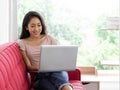 Young asian teen use laptop computer on the red sofa to relax in the living room Royalty Free Stock Photo