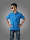 Young Asian teenage boy wearing blue collared shirt and sunglasses standing with hands on hip over grey background, t-shirt Royalty Free Stock Photo