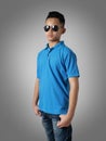 Young Asian teenage boy wearing blue collared shirt and sunglasses standing with hands on hip over grey background, t-shirt Royalty Free Stock Photo