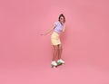 Young asian teenage girl playing on skateboard with wearing wireless headphones listening to music on pink background Royalty Free Stock Photo