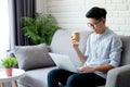 Young Asian teenagers are working, holding a cup of hot coffee and sitting on the sofa at home