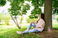 Young Vietnamese woman sitting relaxing in shadow under green tree on sunny day Royalty Free Stock Photo