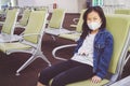 Young Asian tourist girl with mask sitting with distance at the airport