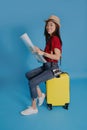 Young Asian traveler sitting on a yellow suitcase. She is looking at the travel map Royalty Free Stock Photo