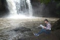 Young Asian traveler woman looking a map in happiness and sitting on a rock of waterfall.