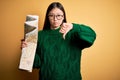 Young asian turist woman looking at city tourist map on a trip over yellow background with angry face, negative sign showing