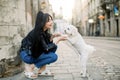 Young Asian urban girl wearing stylish casual clothes, jeans and leather jacket, walks with little cute white dog on the