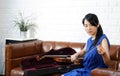 Young asian violinist in blue dress takes care of the instrument after practice session in living room. Rubbing rosin on the