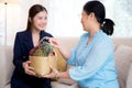 Young asian woman agent insurance visit customer elderly while giving fruit basket in the living room. Royalty Free Stock Photo