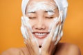 Young Asian woman applying cream on her face and touching face while wearing a bath towel.  on orange background Royalty Free Stock Photo