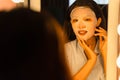 Young Asian woman is applying facial sheet mask on her face and looking at her reflection in the bathroom Royalty Free Stock Photo