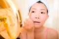 Young Asian woman applying makeup - beautiful and attractive Chinese girl with head towel putting facial make-up at home in the Royalty Free Stock Photo