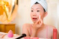 Young Asian woman applying makeup - beautiful and attractive Chinese girl with head towel putting facial make-up at home in the Royalty Free Stock Photo