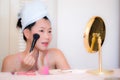 Young Asian woman applying makeup - beautiful and attractive Chinese girl with head towel putting facial make-up at home in the Royalty Free Stock Photo