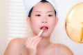 Young Asian woman applying makeup - beautiful and attractive Chinese girl with head towel putting facial make-up at home in the Royalty Free Stock Photo