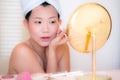 Young Asian woman applying makeup - beautiful and attractive Japanese girl with head towel putting facial make-up at home in the Royalty Free Stock Photo