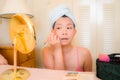 Young Asian woman applying makeup - beautiful and attractive Korean girl with head towel putting facial make-up at home in the Royalty Free Stock Photo