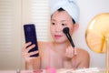 Young Asian woman applying makeup - beautiful and attractive Korean girl with head towel putting facial make-up at home in the Royalty Free Stock Photo