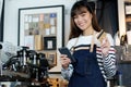 Young asian woman barista using smartphone and holding credit ca