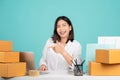 Young Asian woman in casual shirt sit work at desk with a brown cardboard box and point index finger on pc laptop. She using