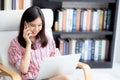 Young asian woman on chair in living room talking smartphone and work from home on laptop computer online. Royalty Free Stock Photo