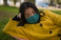 Young Asian woman in city park during covid19 - outdoors lifestyle portrait of happy and pretty Chinese girl in face mask lying Royalty Free Stock Photo