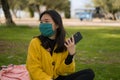 Young Asian woman in city park during covid19 - outdoors lifestyle portrait of happy and pretty Chinese girl in face mask using Royalty Free Stock Photo