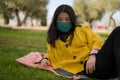 Young Asian woman in city park during covid19 - outdoors lifestyle portrait of happy and pretty Korean girl in face mask lying Royalty Free Stock Photo