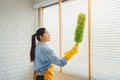Young asian woman cleaning house wiping dust using Feather broom and duster while cleaning on window House keeping concept