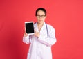 young Asian woman doctor showing the screen of digital tablet dress in white surgical coat standing isolated in red background Royalty Free Stock Photo