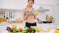 Young Asian woman drink orange juice making salad in the kitchen, beautiful female in sport clothing use organic fruits and Royalty Free Stock Photo