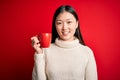 Young asian woman drinking a cup of hot coffee over isolated red background with a happy face standing and smiling with a Royalty Free Stock Photo