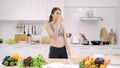 Young Asian woman drinking orange juice in the kitchen, beautiful female in sport clothing use organic fruits lots of nutrition Royalty Free Stock Photo