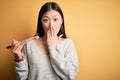 Young asian woman eating japanese food, holding salmon and rice maki sushi using chopsticks cover mouth with hand shocked with Royalty Free Stock Photo