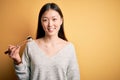 Young asian woman eating japanese food, holding salmon and rice maki sushi using chopsticks with a happy face standing and smiling Royalty Free Stock Photo