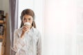 Young Asian woman enjoy listening to music with headphones and holding a hot cup of coffee, happy and relaxing time Royalty Free Stock Photo