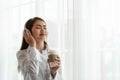 Young Asian woman enjoy listening to music with headphones and holding a hot cup of coffee, happy and relaxing time Royalty Free Stock Photo