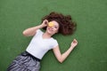 Young Asian woman enjoying the lying on her back on the green grass and hiding her eye with orange piece. Top view