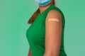 Young Asian woman in facemask with plaster patch on the arm after vaccination  on green background copy space. People got Royalty Free Stock Photo