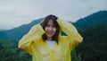 Young Asian woman feeling happy playing rain while wearing raincoat walking near forest. Lifestyle women enjoy and relax in rainy