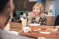 A young asian woman giggles in the middle of eating pizza while her friend tells her some jokes or funny gossip. Friendship