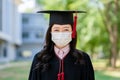 Young asian woman graduate student in a protective medical mask, in a black graduation dress Royalty Free Stock Photo