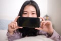 Young Asian woman with hand phone - lifestyle home portrait of happy and beautiful Korean girl on bed posing playful with mobile Royalty Free Stock Photo