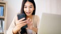 Young asian woman happy working on computer laptop and hand typing chat message on mobile smartphone at home Royalty Free Stock Photo