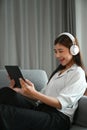 A young Asian woman with headphone enjoying time and sitting on sofa relaxing with tablet. Royalty Free Stock Photo