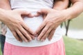 Young asian woman and her husband together caressing her pregnant belly holding their hands in a heart shape on her baby bump. Pr Royalty Free Stock Photo